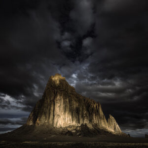 Dappled morning sunlight breaking through the clouds resembling a calico cat on the face of Shiprock