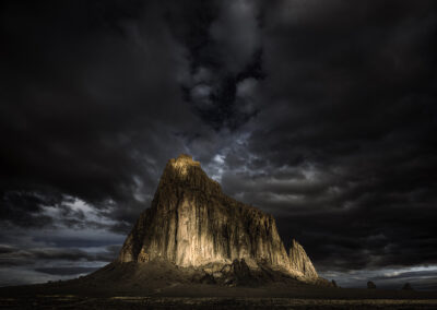 Dappled morning sunlight breaking through the clouds resembling a calico cat on the face of Shiprock